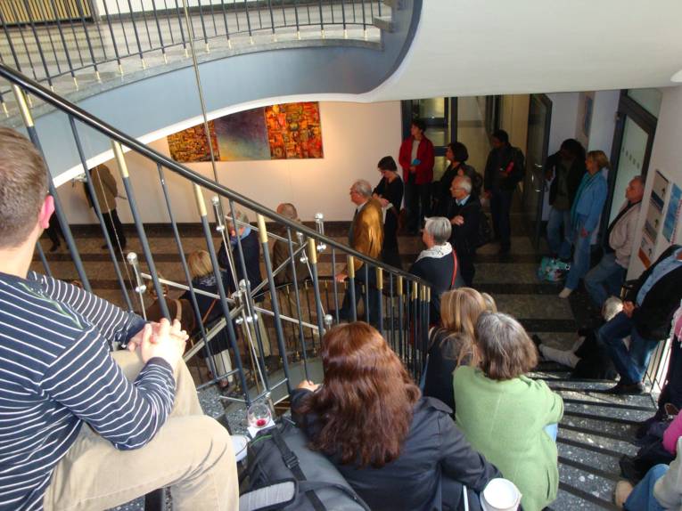 Viele Personen stehen in einem Treppenhaus oder sitzen auf den Treppenstufen.